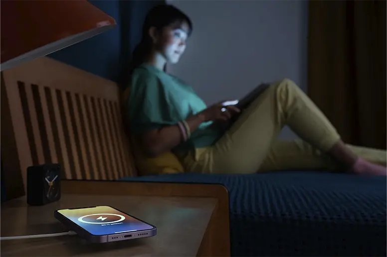 Handy liegt nachts auf einer induktiven Ladestation, Person im Hintergrund sitzt auf dem Bett