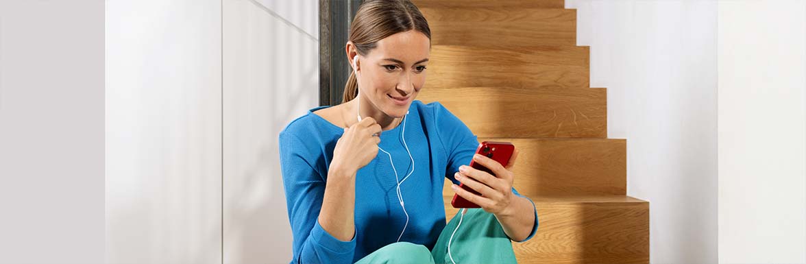 Person mit Handy in der Hand, welches mit kabelgebundenen Kopfhörern verbunden ist.