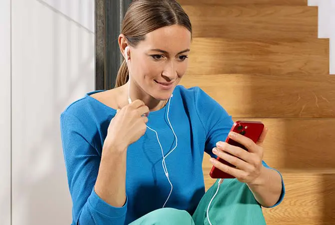 Person mit Handy in der Hand, welches mit kabelgebundenen Kopfhörern verbunden ist.