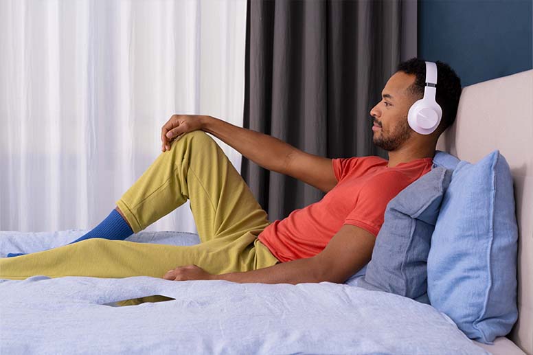 Person sitzt entspannt mit Kopfhörern im Bett.