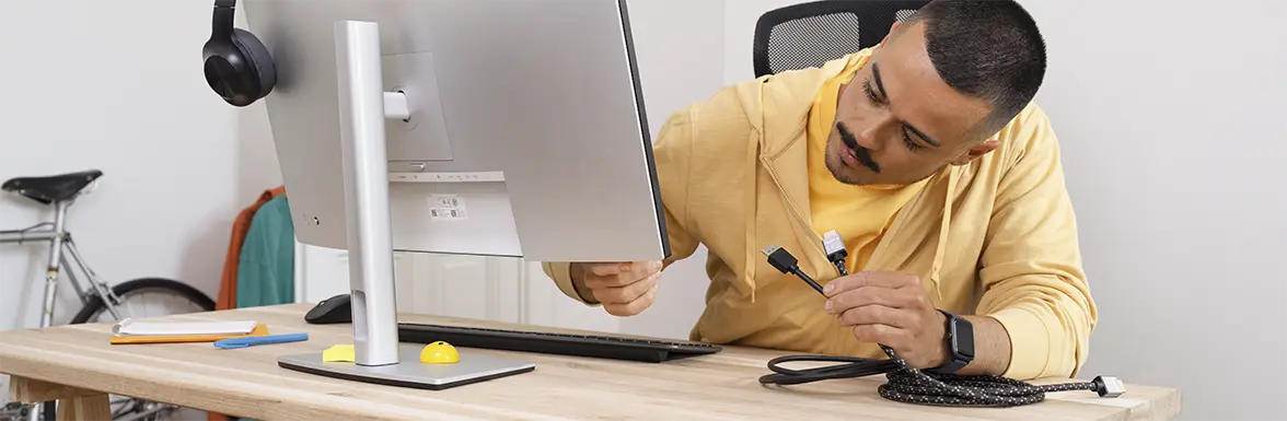 Person prüft Monitoranschlüsse und hält unterschiedliche Kabel in der Hand.