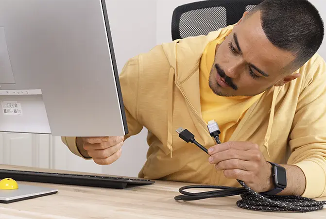 Person prüft Monitoranschlüsse und hält unterschiedliche Kabel in der Hand.