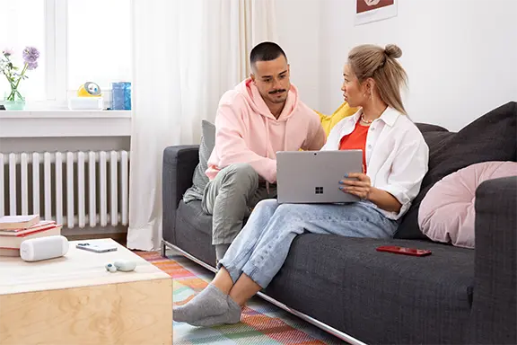 Person sitzt auf der Couch vor einem geöffneten Notebook.