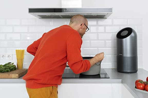 Person kocht während ein Luftreiniger neben der Herdplatte steht.