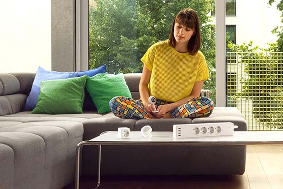 Glückliche Person am Wohnzimmertisch. Vor ihr liegen verschiedene Smart Home Geräte, die für Mietwohnungen erlaubt sind.