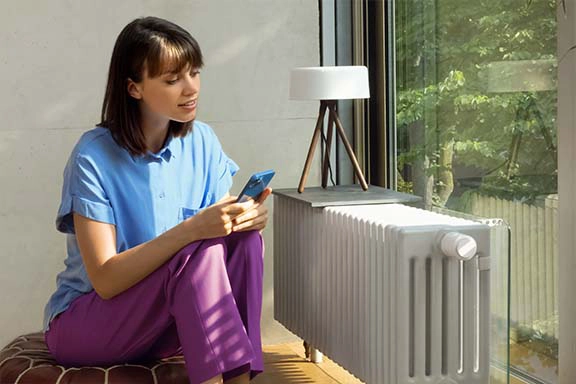 Person vor einem Heizkörper mit Smarthome-Thermostat.