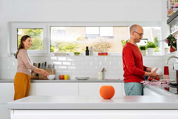Personen stehen in der Küche, im Vordergrund steht eine Siri von Apple.