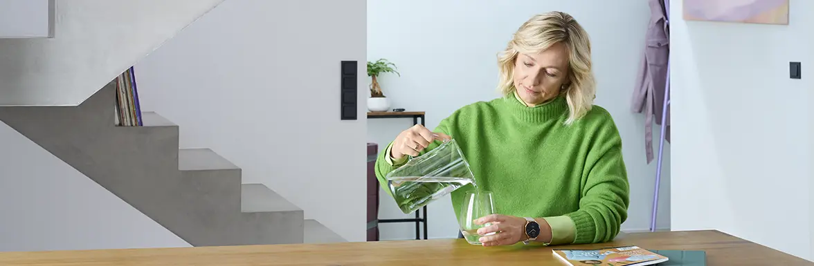 Person gießt Wasser in ein Glas.