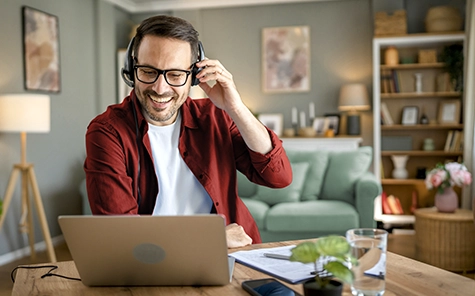 Ein Mann arbeitet im Home Office in seinem Wohnzimmer an seinem Laptop und telefoniert über ein Headset.