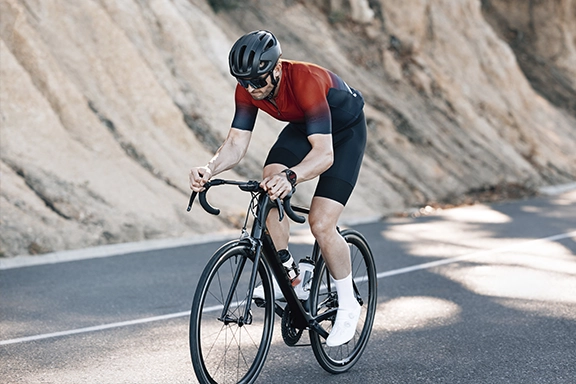 Ein Mann fährt auf einem Rennrad eine Bergstraße entlang, mit einer Hama Smartwatch am Handgelenk.