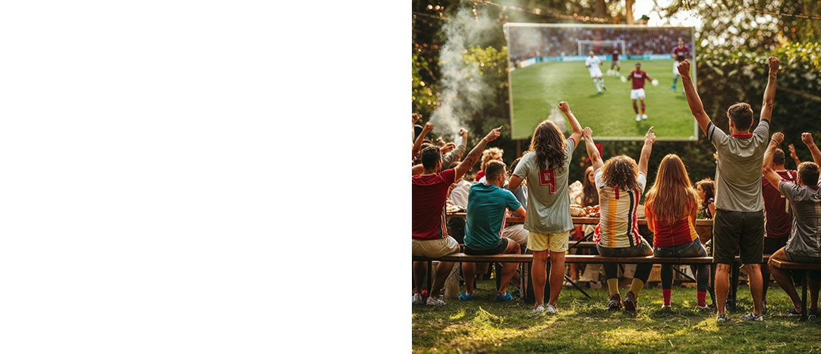 Eine Gruppe junger Leute sitzen und stehen bei sommerlichen Temperaturen im Freien und bejubeln ein Fußball-Spiel, dass live auf einen großen Fernseher übertragen wird.