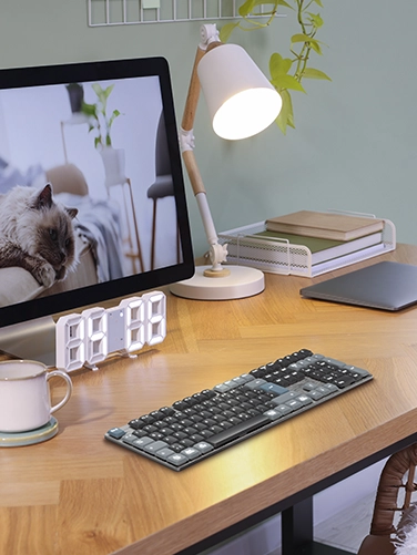 Auf einem Schreibtisch aus Holz liegt das Hama Multi-Device-Tastatur "WK-800", sowie ein Tablet, Stehlampe, Digitaluhr und Bildschirm