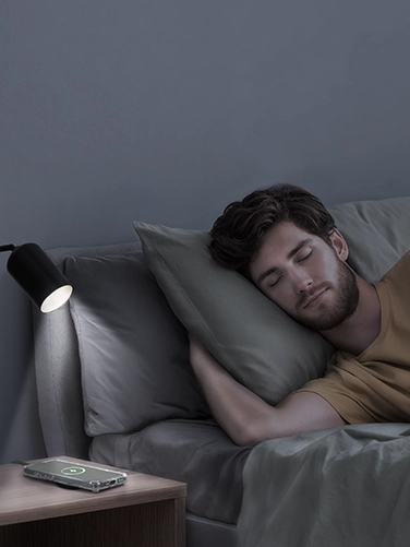 Man liegt schlafend im Bett während das Handy auf dem Nachtkästchen kabellos lädt.