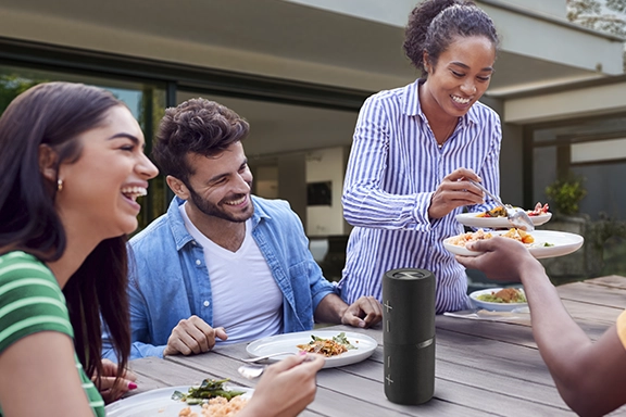 Mehrere Personen sitzen zusammen bei einem Grillabend im Garten und die Bluetooth-Box 4.0 steht auf dem Tisch.