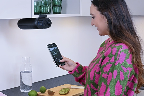 Eine Frau steht in der Küche und verbindet ihr Handy per Bluetooth mit dem Hama Unterbauradio.