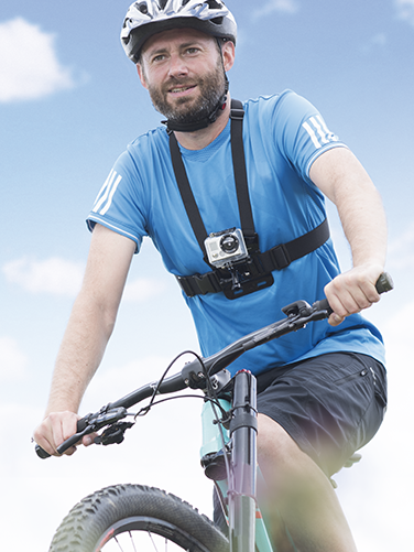Ein Mann in T-Shirt und kurzer Hose fährt Rad und trägt seine Action-Kamera mit dem Hama Brustgurt für GoPro